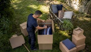 Un déménageur range soigneusement des vêtements sur un carton penderie pour faciliter leur transport.
