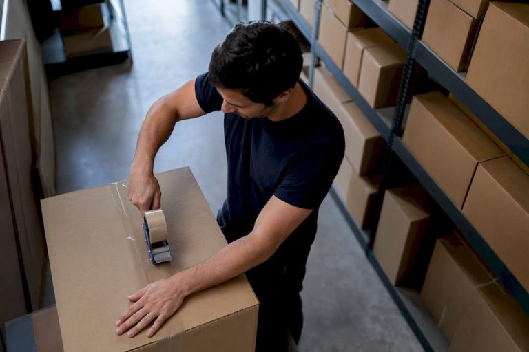 On ferme soigneusement des cartons à l’aide de ruban adhésif dans une pièce remplie de boîtes prêtes à être entreposées.
